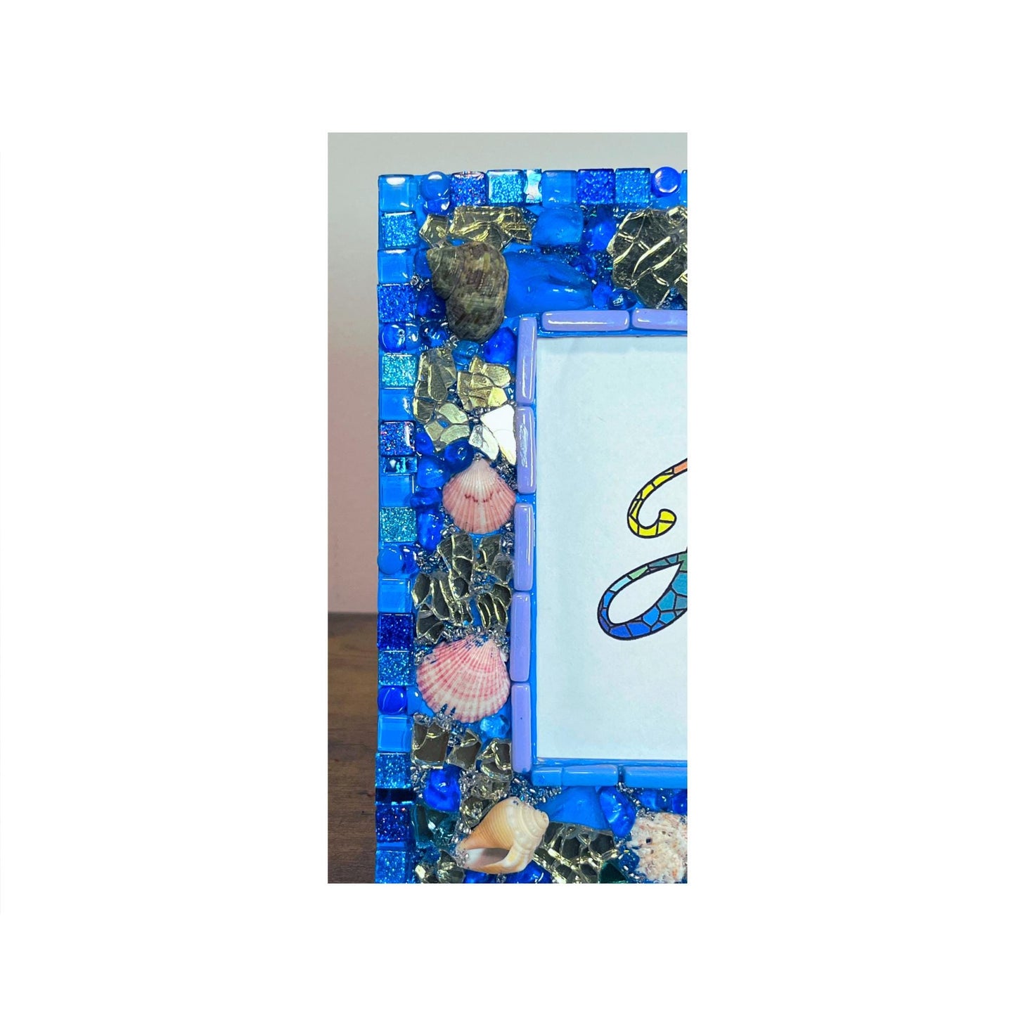 left side view:
Front of five by seven photo frame with edges done in blue shades of glass and metallic tiles, beach glass, glass, rounds gold reflective glass, Natural Sea Shells, Grouted with blue, silver and gold seed beads mixed with resin