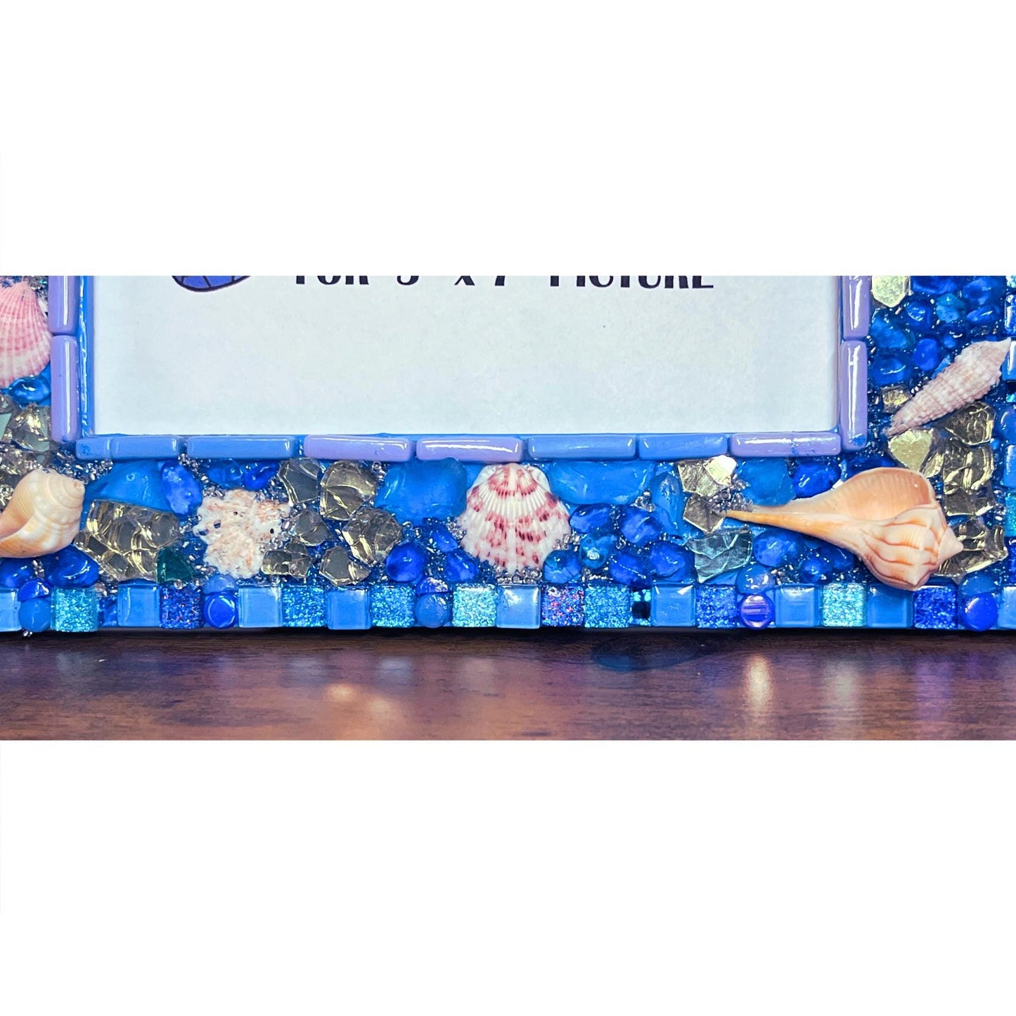 bottom close up:
of five by seven photo frame with edges done in blue shades of glass and metallic tiles, beach glass, glass, rounds gold reflective glass, Natural Sea Shells, Grouted with blue, silver and gold seed beads mixed with resin
