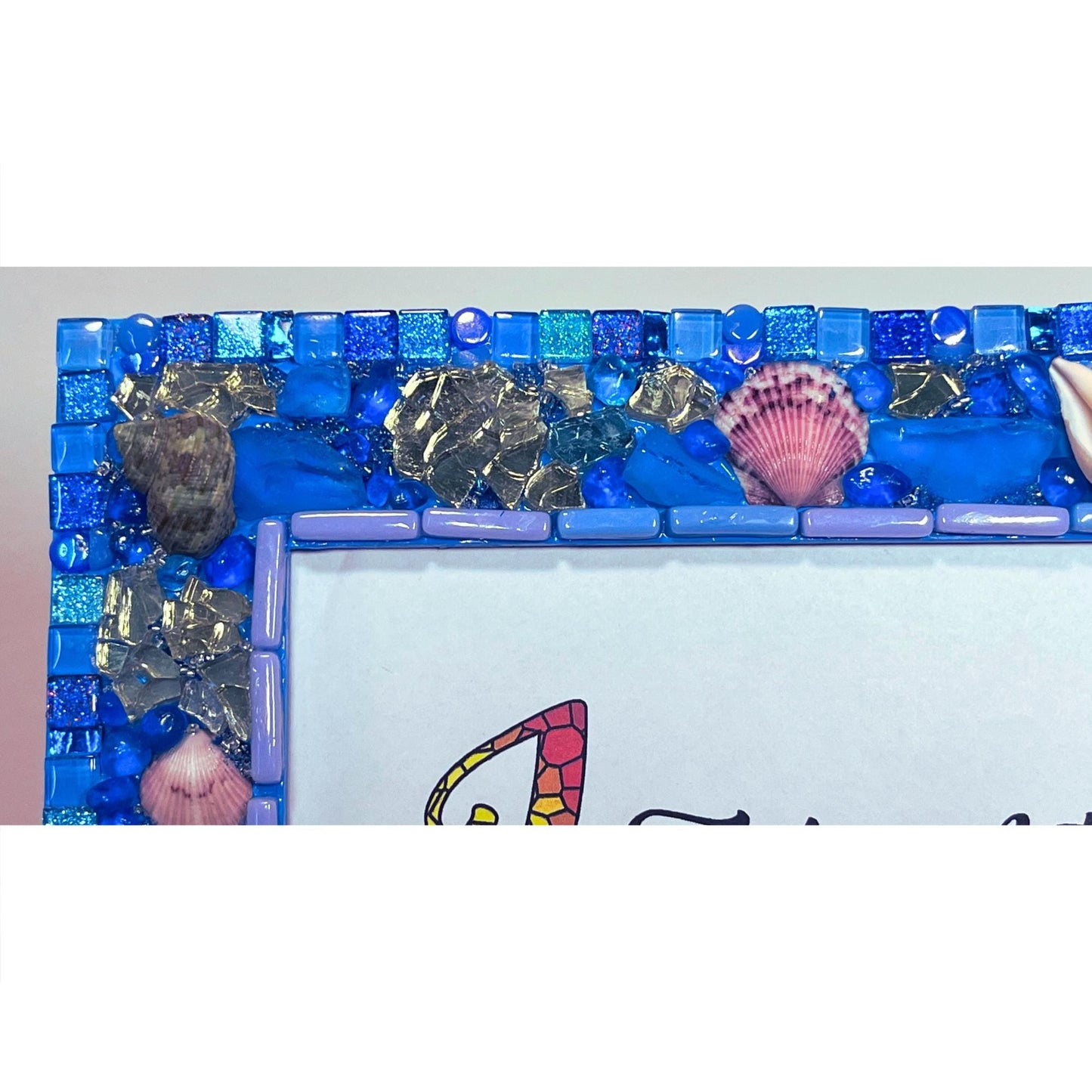 top left close-up:
Front of five by seven photo frame with edges done in blue shades of glass and metallic tiles, beach glass, glass, rounds gold reflective glass, Natural Sea Shells, Grouted with blue, silver and gold seed beads mixed with resin