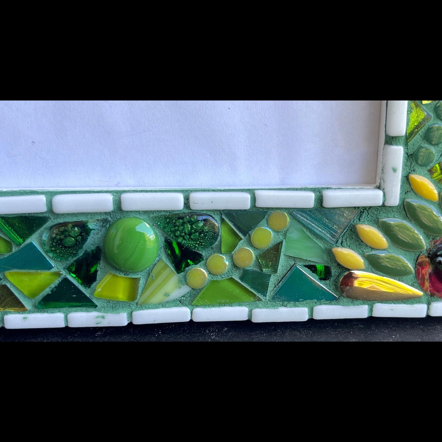 bottom right close up:
5 x 7 Photo frame is shades of green with ceramic leaves, glass beads and tiles. White Thin subway tiles border the inner and outer borders of the frame. Gold Accents and ladybug fused glass in the four corners.  The background grout color is medium green.