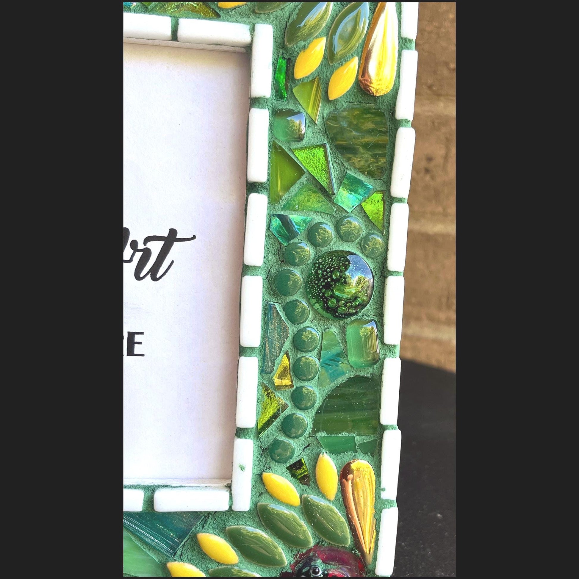 right side view:
5 x 7 Photo frame is shades of green with ceramic leaves, glass beads and tiles. White Thin subway tiles border the inner and outer borders of the frame. Gold Accents and ladybug fused glass in the four corners.  The background grout color is medium green.