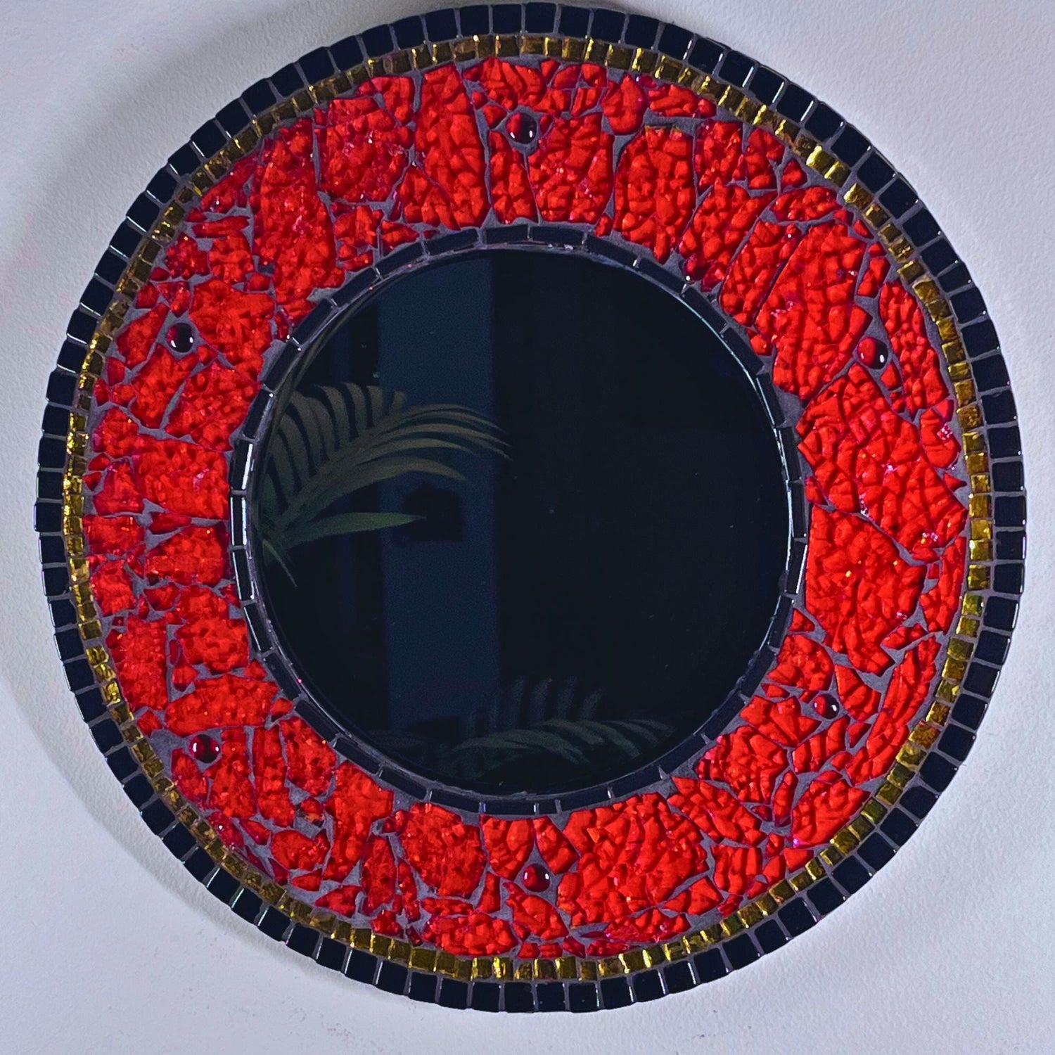 14 inch wood round with 8 inch beveled mirror.  Outside perimeter in black glass tiles outlined with gold mirror tile.  The center mirror is outlined in thin black glass tiles.  The remainder of the mirror is in red hand-tinted tempered glass,  Under the translucent glass are layers of fabric ribbon, glitters and foils