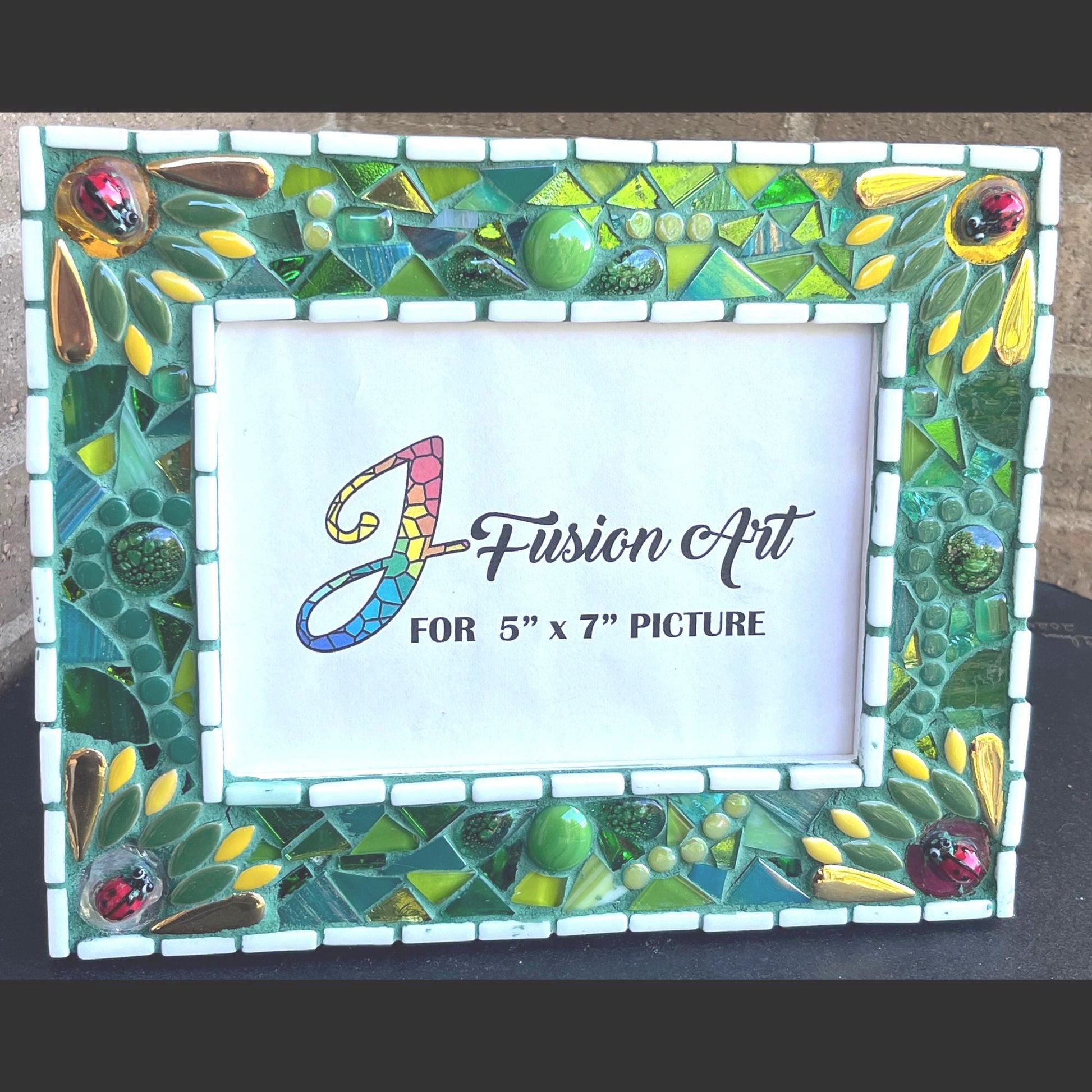 Front View:
5 x 7 Photo frame is shades of green with ceramic leaves, glass beads and tiles. White Thin subway tiles border the inner and outer borders of the frame. Gold Accents and ladybug fused glass in the four corners.   The background grout color is medium green.