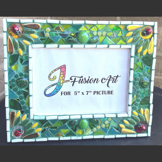 Front View:
5 x 7 Photo frame is shades of green with ceramic leaves, glass beads and tiles. White Thin subway tiles border the inner and outer borders of the frame. Gold Accents and ladybug fused glass in the four corners.   The background grout color is medium green.